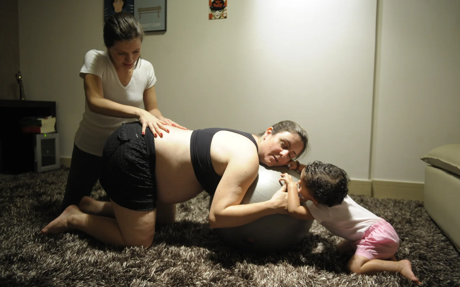 Zwangere vrouw leunt op een oefenbal terwijl een doula haar onderrug ondersteunt