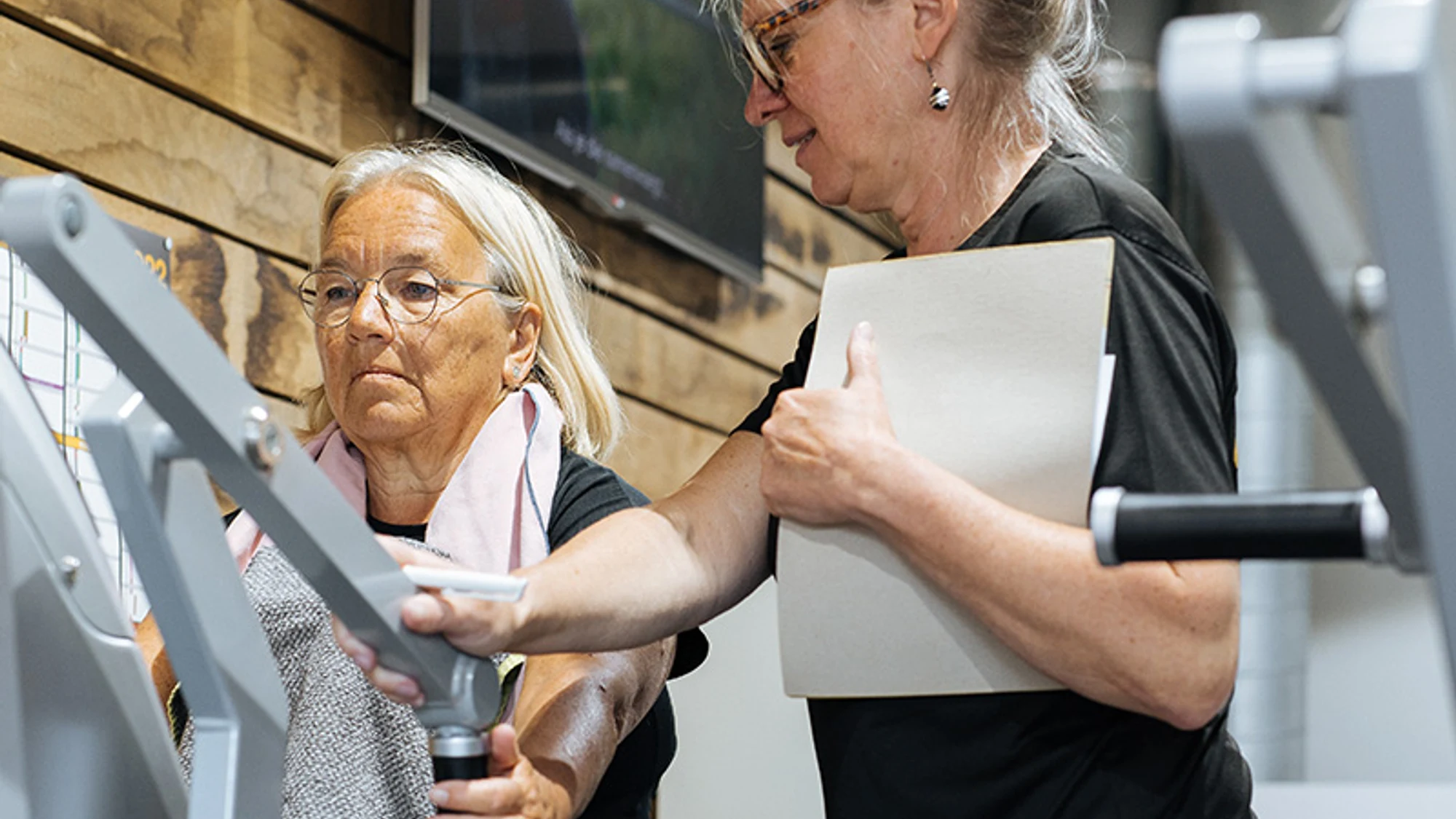 Coach begeleidt vrouw tijdens krachttraining in een kleinschalige fitnessclub